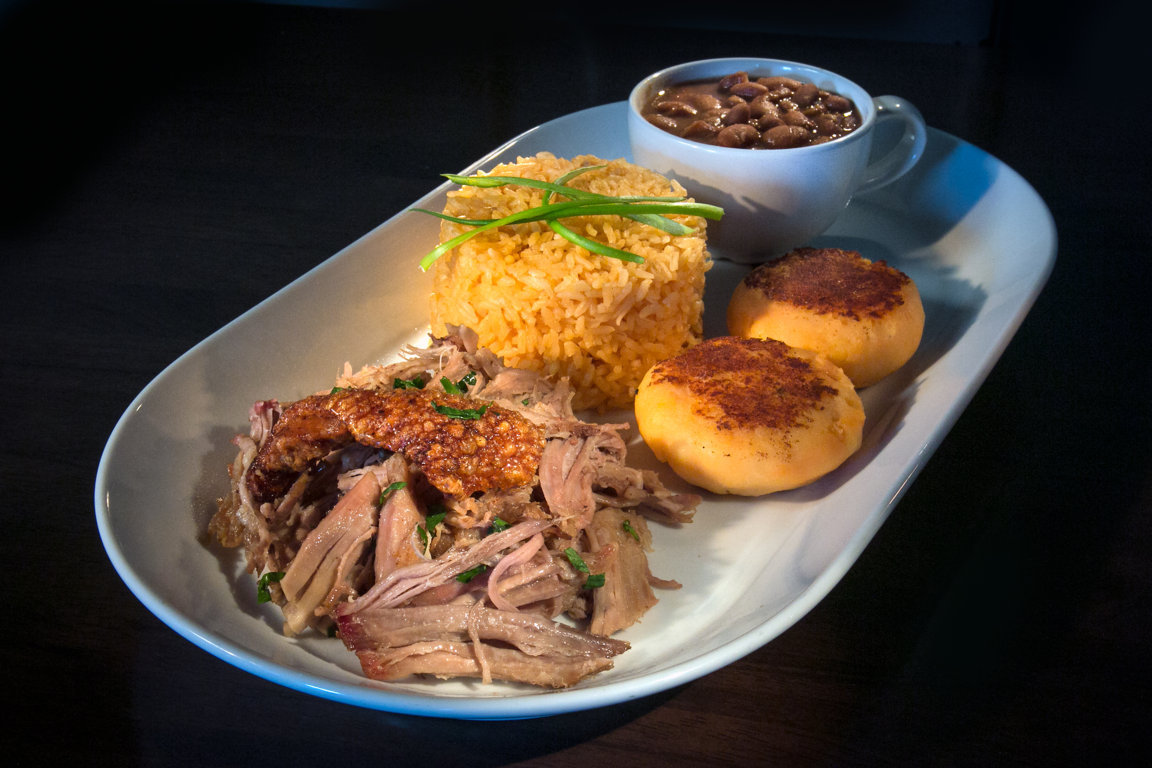 Pernil: Slow-roasted pulled pork shoulder served with rice, beans, and tostones or sweet plantain. 